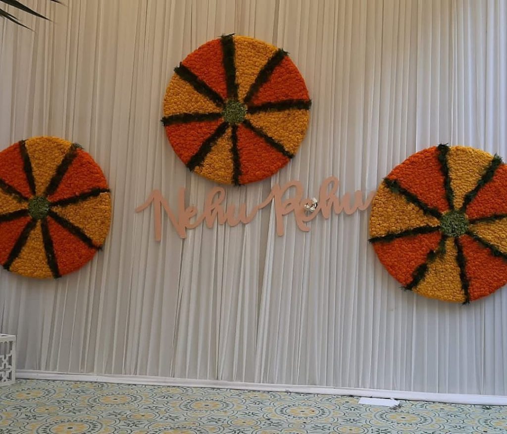 white drapes and circular mariigold floral wheel with pastel nehupreet text for haldi backdrop